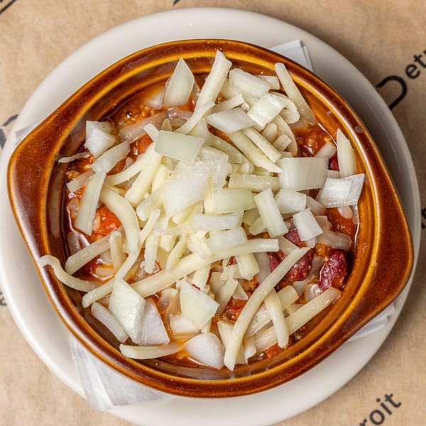 A bowl of CD Top Shelf chili, topped with shredded cheese and diced white onions.