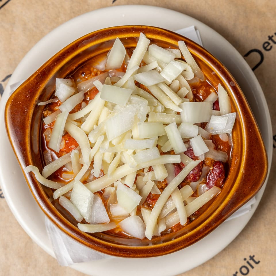 A bowl of CD Top Shelf chili, topped with shredded cheese and diced white onions.