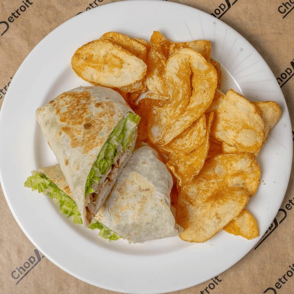A chicken wrap with lettuce and a side of golden potato chips on a white plate.