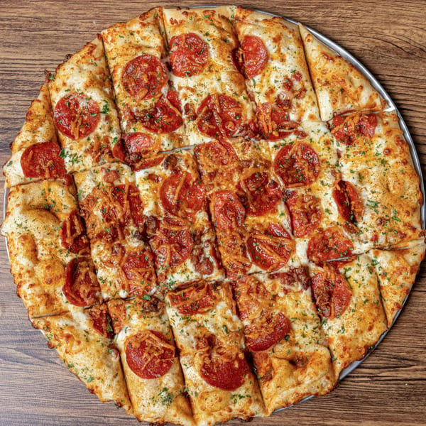 Overhead view of a large, rectangular pepperoni pizza, cut into squares, on a wooden table.