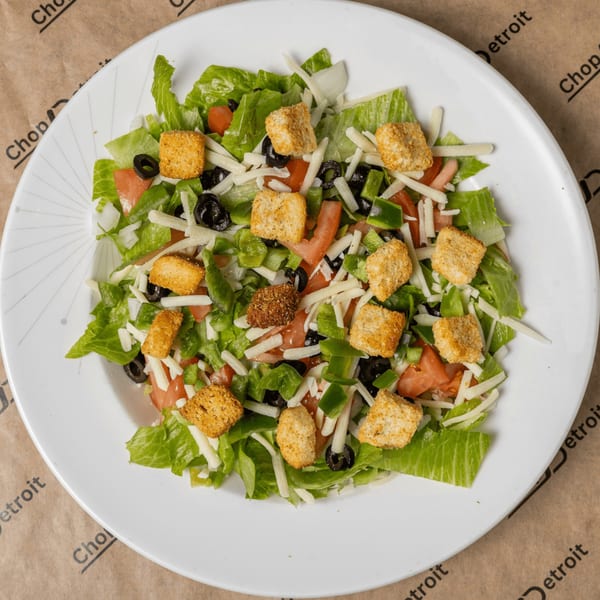 A fresh garden salad with lettuce, tomatoes, green peppers, olives, cheese, and croutons.