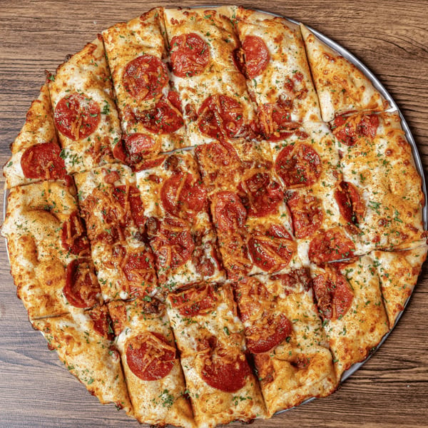 A large, round pepperoni pizza, cut into squares, on a metal pan atop a wooden table.