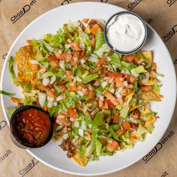 A plate of CD Top Shelf nachos with ground beef, lettuce, tomatoes, jalapeños, and onions, with sides of salsa and sour cream.