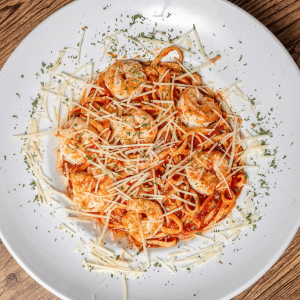 Shrimp pasta with red sauce, shredded cheese, and parsley on a white plate.