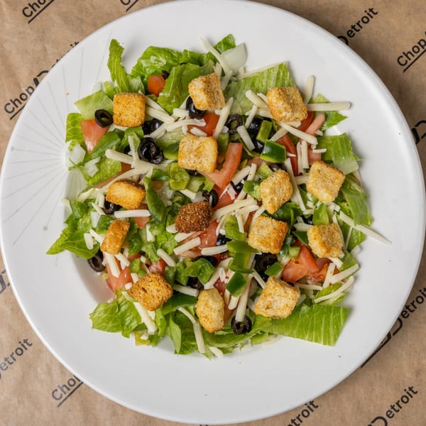 Fresh garden salad with lettuce, tomatoes, green peppers, black olives, shredded cheese, and croutons.