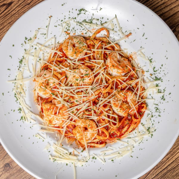 Shrimp pasta with red sauce, topped with shredded cheese and parsley on a white plate.