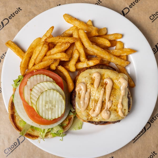 CD Top Shelf burger with melted cheese and special sauce, topped with lettuce, tomato, onion, and pickles, served with fries.