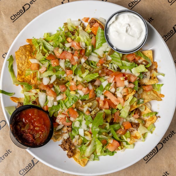 A large plate of CD Top Shelf nachos with ground beef, lettuce, tomatoes, onions, jalapeños, salsa, and sour cream.