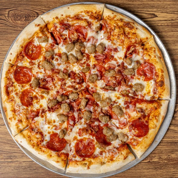 A sliced CD Top Shelf pizza with pepperoni, sausage, and bacon on a wooden table.