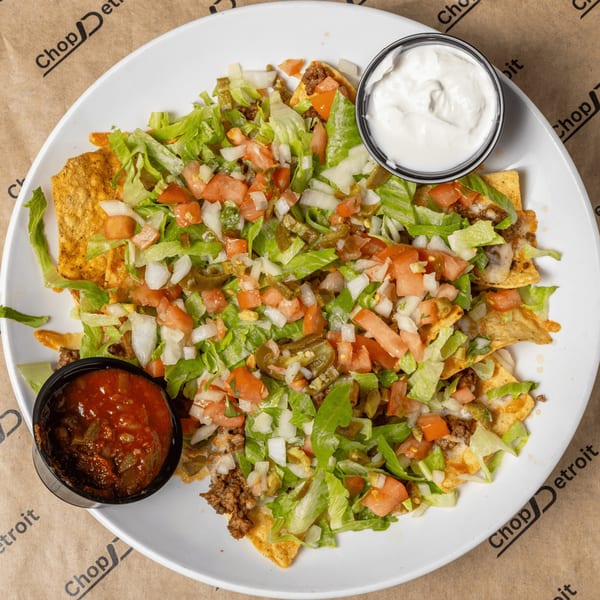 A large plate of CD Top Shelf nachos with ground beef, lettuce, tomatoes, onions, and jalapeños.