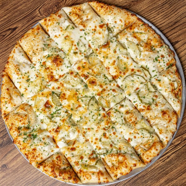 Round CD Top Shelf pickle pizza, cut into strips, with melted cheese and parsley on a wooden table.